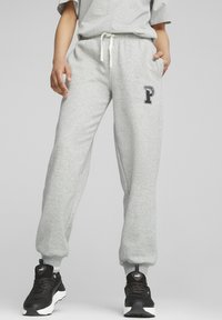 Pantalones de chándal grises de tela suave con un corte relajado, puños elásticos, cintura con cordón y un logotipo impreso en el muslo izquierdo.
