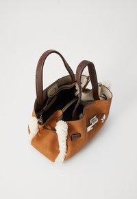 Sac en suède taupe avec des poignées marron foncé, bordure en shearling blanc, ouverture en haut et détails en boucle argentée sur fond blanc.
