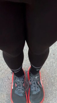 Leggings de sport noirs assortis à des chaussures noires avec des accents rouges, des semelles texturées et des lacets gris, sur une surface claire.