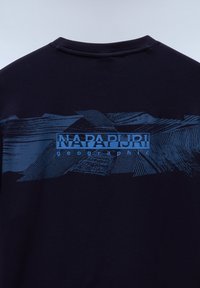 T-shirt bleu marine avec un graphique texturé bleu affichant des motifs de montagne et le nom de la marque "NAPAPIJRI" en lettres bien en vue.