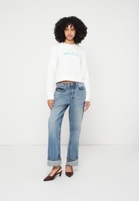 Λευκό cropped sweatshirt με πράσινο κεντητό κείμενο, συνδυασμένο με ανοιχτό μπλε παντελόνι wide-leg που έχει διπλωμένα τα μπατζάκια, και μπορντό γόβες σε σχήμα βέλους.