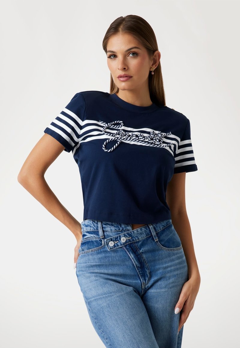 T-shirt a maniche corte color navy con righe orizzontali bianche e dettagli in corda sulla parte frontale. Abbinato a jeans a vita alta di colore blu chiaro.