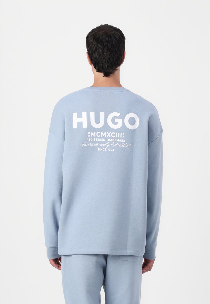 Világoskék, over size fazonú pulóver hosszú ujjal. A hátsó részen nagy, fehér színű "HUGO" felirat és további márkáz�ás található alatta. Puha, textúrált anyag.