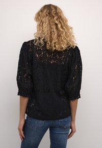 Black lace blouse with puffed sleeves, featuring floral patterns and a semi-sheer texture. Paired with blue denim jeans, viewed from the back.