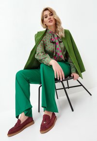 Lysegrønne bukser parret med en prikket bluse i grøn og pink, suppleret med en grøn blazer og bordeaux ruskinds loafers.
