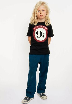 Black t-shirt with "PLATFORM 9¾" graphic in red and white, paired with dark teal sweatpants and navy sneakers with white soles.