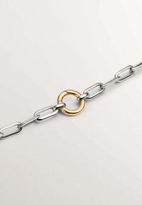 Cadena de metal plateado con eslabones alargados y un anillo central dorado. El anillo dorado es liso, contrastando con los brillantes eslabones plateados.