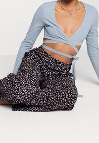 Jasnoniebieski top z długim rękawem i wąskimi tasiemkami, w połączeniu z czarnymi spodniami w kwiatowy wzór, z elastycznym paskiem w talii i falbanami.