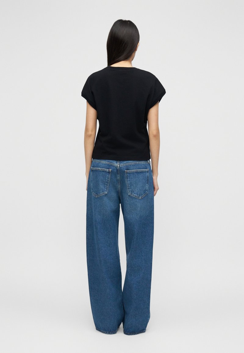 Haut noir à manches courtes associé à un jean à jambes larges bleu clair. Le haut présente un col rond, et le jean possède de grandes poches arrière.