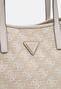 Sac fourre-tout beige tissé avec une surface texturée, des accents en cuir et un logo triangulaire doré à l'avant.