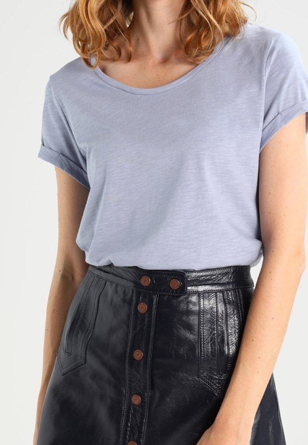 Femme portant un t-shirt bleu clair à manches courtes, rentré dans une jupe en cuir noire taille haute à boutons.