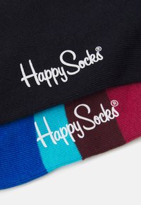 Chaussettes Happy en noir, bleu et bordeaux avec une finition texturée ; présente un logo blanc brodé sur chaque paire. Design à rayures contrastées.