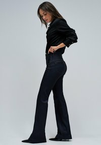 Vaqueros acampanados de color azul oscuro hechos de mezclilla, con una cintura alta, costuras en contraste y un acabado suave. Combinados con una camiseta negra.