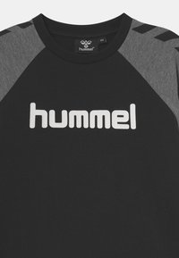 Sort t-shirt med kort ærme og grå raglan-ærmer, der har et stort hvidt "hummel" logo henover brystet og en rund halsudskæring.
