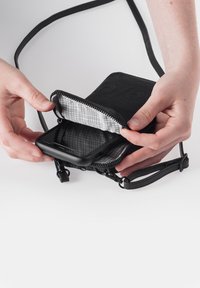 Black crossbody phone pouch with a zip closure, featuring a grid-patterned lining, and an adjustable strap. Phone visible inside.