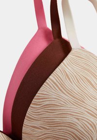 Snyggt set med en beige mönstrad kupa med vågiga linjer, en brun remsa och rosa band. Materialen verkar texturerade och mjuka.