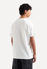 T-shirt in cotone bianco con maniche corte, collo rotondo e vestibilità comoda. La vista posteriore mostra una texture liscia e senza motivi.