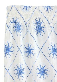 Vitt tyg med blå solstråle-mönster, som har en texturerad, rynkad yta. Elastisk toppkant förbättrar passformen. Geometriska designelement finns.