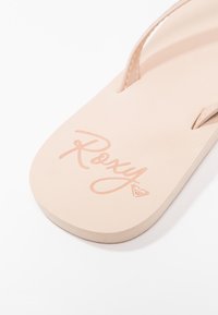 Flip-flop Roxy în roz deschis din cauciuc, cu o talpă plată și un logo embosat pe talpa interioară. Bretelele sunt minime, cu un finisaj neted.