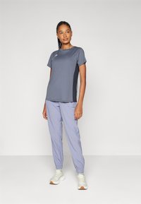 Grå sports T-skjorte med korte ermer, kombinert med lyse lilla bukser med elastisk midje og hvite joggesko med lys brun såle.