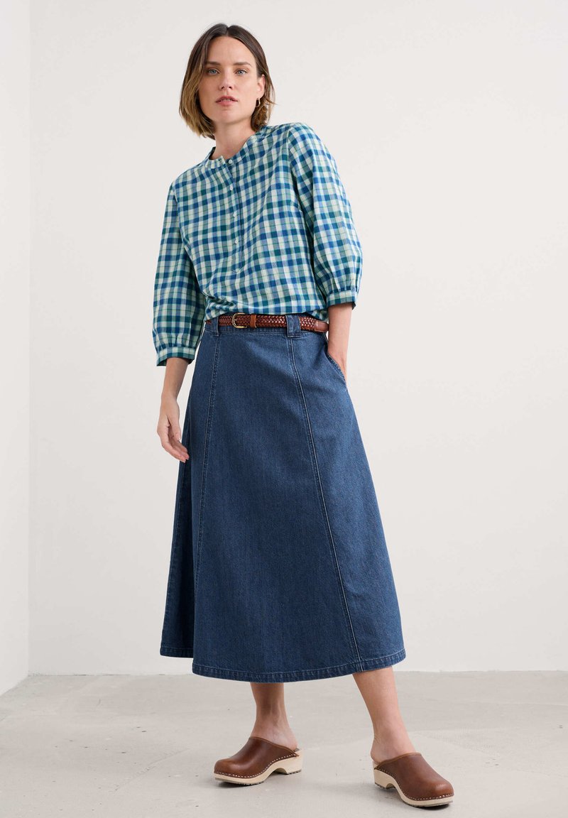 Blau- und grünkariertes Blusenshirt mit Dreiviertelärmeln, kombiniert mit einem langen Jeansrock und braunen Clogs mit Holzsohle.