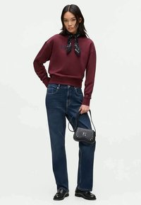 Sweatshirt bordeaux com um lenço de pescoço, emparelhado com jeans de perna reta azul escuro. Acessorizado com uma mala preta com tachas e sapatos pretos.