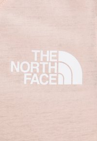 Světle růžová látka má velké bílé logo s zakřivenými liniemi, na kterém je tučně napsáno "THE NORTH FACE". Hladký povrch.
