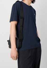 T-shirt in cotone blu navy con maniche corte, abbinato a una borsa a tracolla nera caratterizzata da un design elegante, texture liscia e tracolla regolabile.