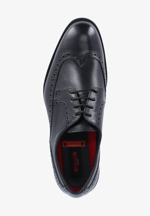 Black leather dress shoe featuring brogue detailing, lace-up design, and a red cushioned interior. Smooth texture and sleek shape.