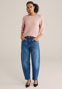 Pulover roz deschis tricotat cu un model texturat în formă de diamant și mâneci trei sferturi, asortat cu blugi largi cu talie înaltă, din denim albastru.