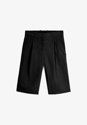 Mustat shortsit, jotka on valmistettu tekstiilistä, jossa on matta pinta. Shortsien etuosa on tasainen, niissä on kaksi sivutaskua ja ne ovat väljempiä. Ei näkyvää metalliosaa tai kuvioita.