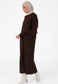Hnědý, oversized pletený svetr s dlouhými rukávy a uvolněným střihem. Ozdobený jemným třpytem. V kombinaci se světlými vysokými botami.