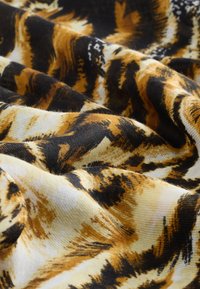 Weicher Stoff mit schwarzen, braunen und beigen Tigermuster-Streifen, in Nahaufnahme mit Biegungen und Falten gezeigt.