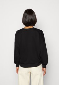 Sudadera negra con hombros caídos, puños acanalados y dobladillo. El material parece suave con una textura lisa. La vista trasera muestra un diseño de cuello redondo.