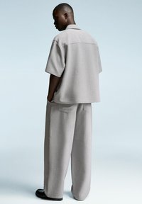 Cămașă scurtă de culoare gri deschis cu mâneci scurte și pantaloni largi din țesătură texturată. Cămașa are un guler plat, detalii subtile de cusătură și un croi lejer.