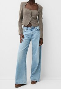 Brun rutigt kort blazer med tre knappar och fyrkantig halsringning, tillsammans med ljusblå vida jeans och bruna loafers.