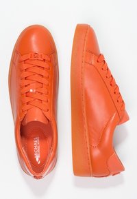 Oranžové kožené tenisky s hladkým povrchem, zaoblenou špičkou, plochou gumovou podrážkou a kontrastními šněrováním. Vnitřní podšívka odpovídá barvě exteriéru.