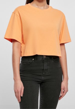 Beslået orange bomulds T-shirt med korte ærmer og rund halsudskæring, parret med højttalende sorte denimjeans.