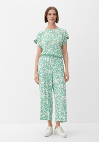 Lichtgroene twee-delige outfit met een losse blouse en wijde broek met een wit bloemenpatroon, gemaakt van zachte stof, gecombineerd met witte sneakers.