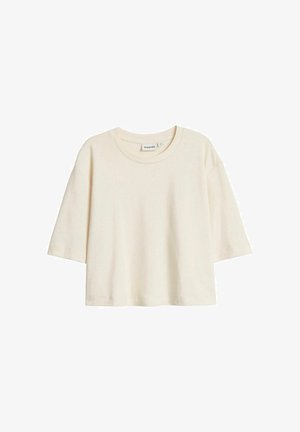 Kremowy, krótki rękaw, sweter o pudełkowym kroju z okrągłym dekoltem i widoczną metką marki wewnątrz kołnierza.