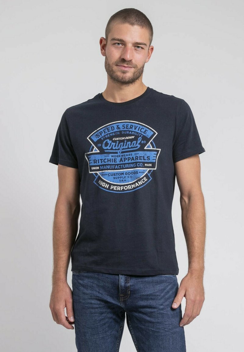 T-shirt en coton noir avec un design graphique bleu comportant du texte et des logos. Le t-shirt a des manches courtes et un col rond, associé à un jean bleu.