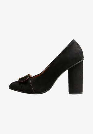 Chaussure à talon haut en suede noir avec un bout arrondi et un détail en nœud. Le talon carré offre de la stabilité, avec une texture lisse et une finition mate.