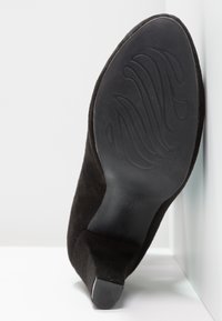 Black suede high heel shoe with a textured sole and a sleek, tapered design. Size 37 embossed on the sole. Side view showing heel angle.