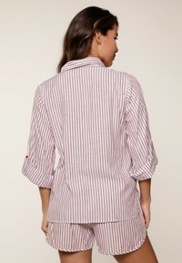 Completo pigiama a righe in rosso e bianco, composto da una camicia con colletto e maniche arrotolate e pantaloni corti abbinati, realizzato in tessuto di cotone leggero.