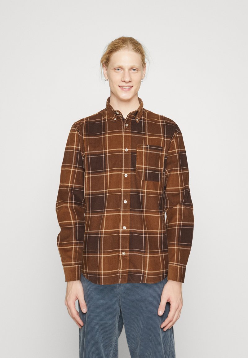 Bruine geruite overhemd van flanel, met lichte en donkere bruine vierkanten en witte accenten. Met een button-down kraag en een enkele borstzak.