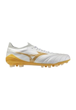 Botas de fútbol blancas y doradas con cordones, parte superior texturizada y tacos moldeados para jugar en terreno firme, mostradas de perfil derecho.