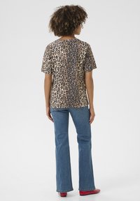 Leopard print short-sleeve shirt, lightweight fabric, relaxed fit. Paired with blue flared jeans and red shoes. Back view with natural hair.