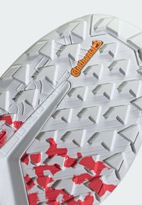 White traction sole with textured pattern and red paint splatter. Features include angled lugs and a visible orange logo.