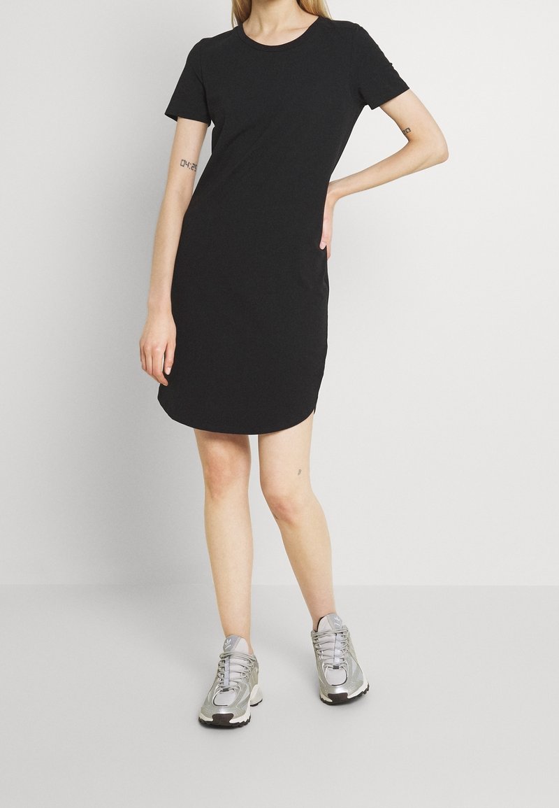 Robe noire à manches courtes avec un encolure ronde, texture douce et ourlet arrondi. Portée avec des baskets de sport argentées.