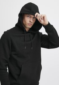 Black hoodie with a front kangaroo pocket, adjustable drawstring hood, embossed "TOKYO" design, and smooth fabric texture.